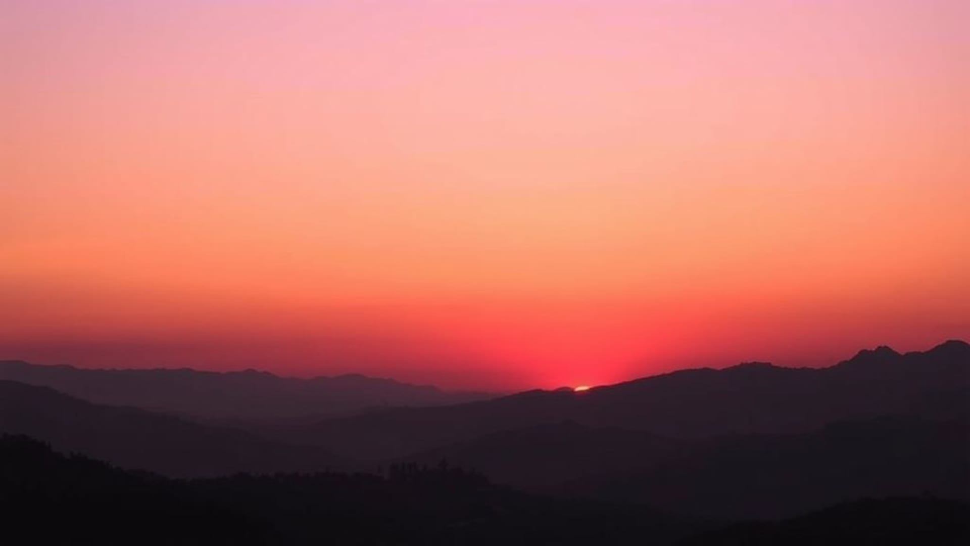silhouettes de montagnes au coucher du soleil couleurs chaudes dégradé de ciel violet rose orange crépuscule paysage calme nature horizon paisible cinématographique