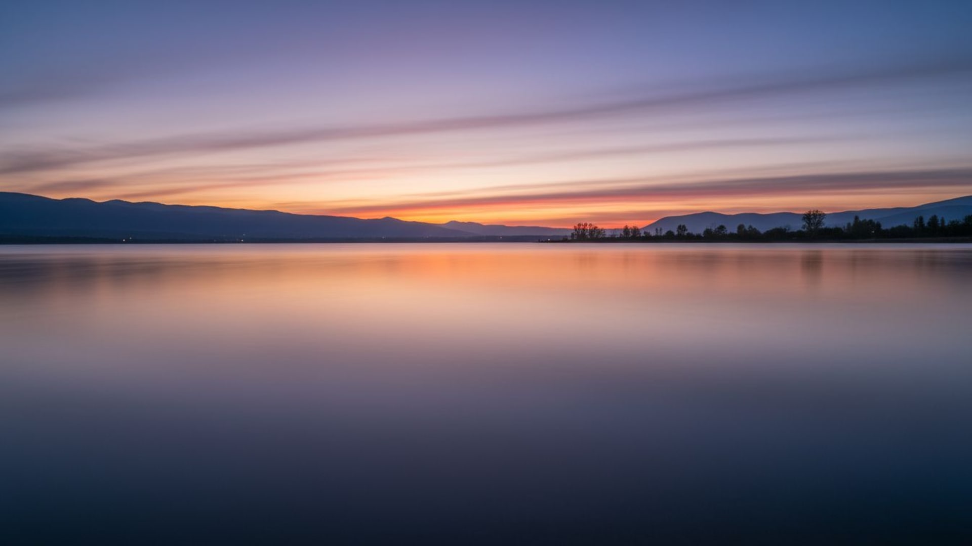 Reflet de l'eau sur le lac au coucher du soleil, exposition longue, vagues lisses, paysage tranquille, fond ecran zen et calme.