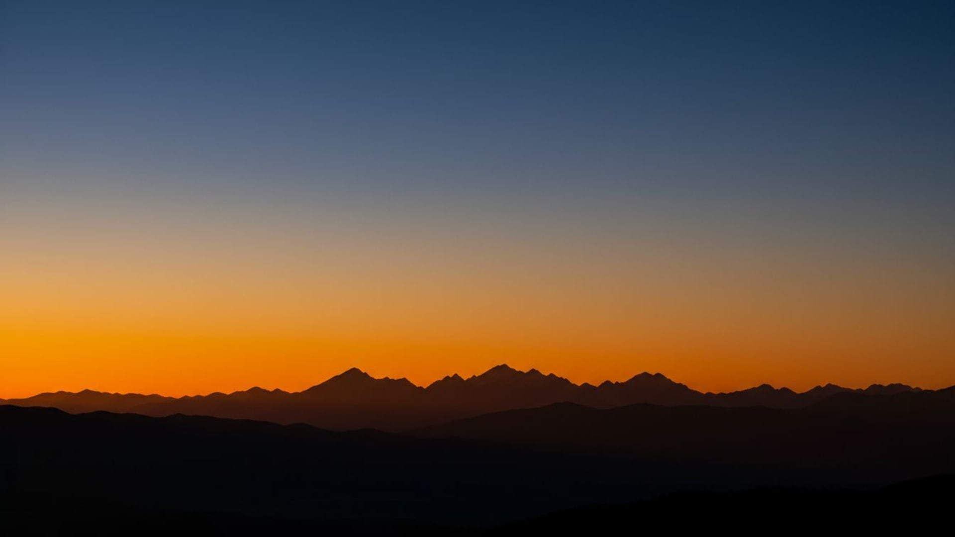 Dégradé de coucher de soleil silhouette de montagne tons chauds ciel bleu froid fond d'écran