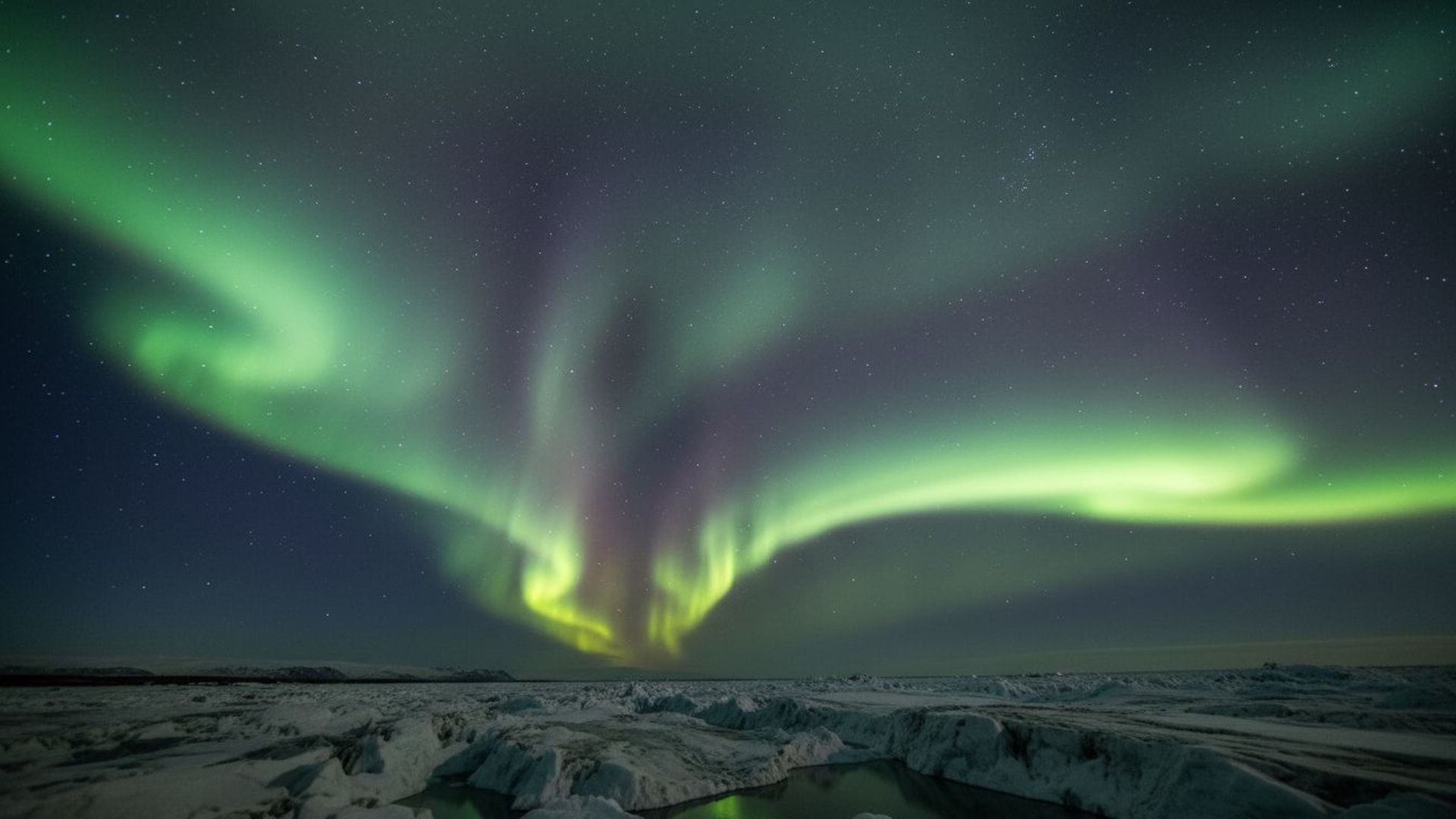 L'aurore boréale illumine le ciel nocturne comme des rideaux de lumière vert clair et violet, avec des étoiles et une glace sombre.